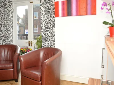 Patient lounge with brown leather tub chairs and a sash window